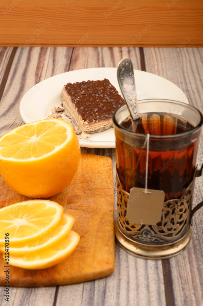 Φωτογραφία Tea in a faceted glass in a vintage Cup holder, sliced lemon on a Board and a piece of waffle cake on a white plate on a wooden background