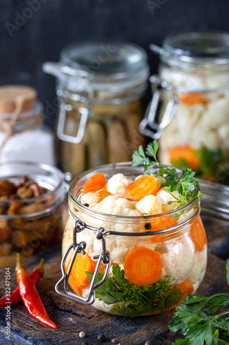 Pickled cauliflower with carrots in a glass jar on a dark wooden table. Fermented food.