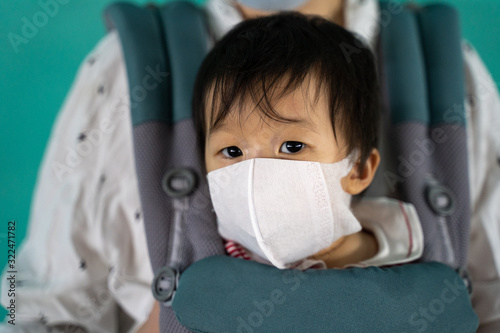 Asian baby with mother in baby carry,baby is wearing a protection mask against air pollution and Wuhan corona virus before flight in terminal DonMuang airport,Bangkok, Thailand. photo