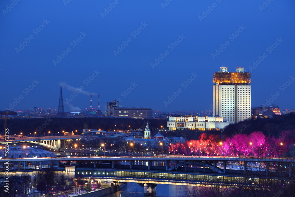Moscow / Russia – 03 07 2019: House of Presidium of the Academy of Sciences, Moscow river with Metro bridge and red illuminated trees at winter night, view from Vorobyovy Hill Observation deck