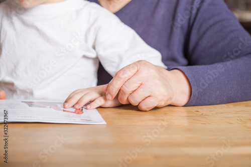 hands mature woman (80 years old) with her great-grandson at home, reading educational book together