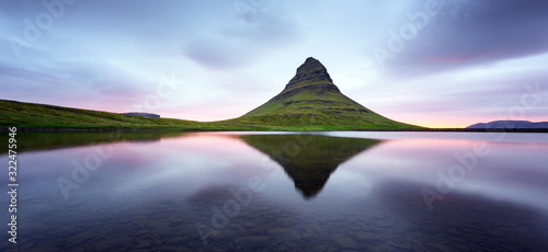 Panoramical landscape with Kirkjufell mountain  clear lake and cloudscape in sunrising sky