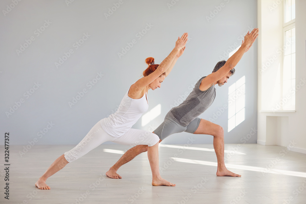 Naklejka premium Yoga for health. A man and a woman in sportswear are practicing yoga in a bright classroom.