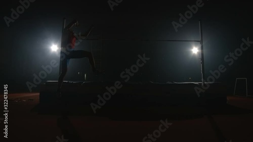 Slow motion: Male athlete high jump and knocked down the bar on a dark background in the spotlight photo