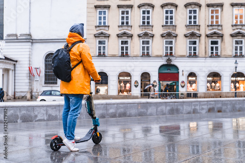 Photography man in yellow raincoat riding by city street at electric scooter