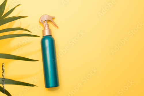 Sunblock spray green bottle on yellow background with palm leaf with a copy space photo