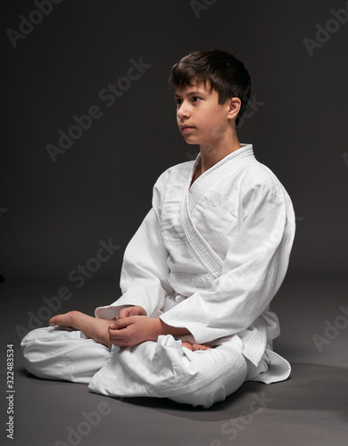 portrait of a teenager dressed in martial arts clothing poses on a dark gray background, a sports concept