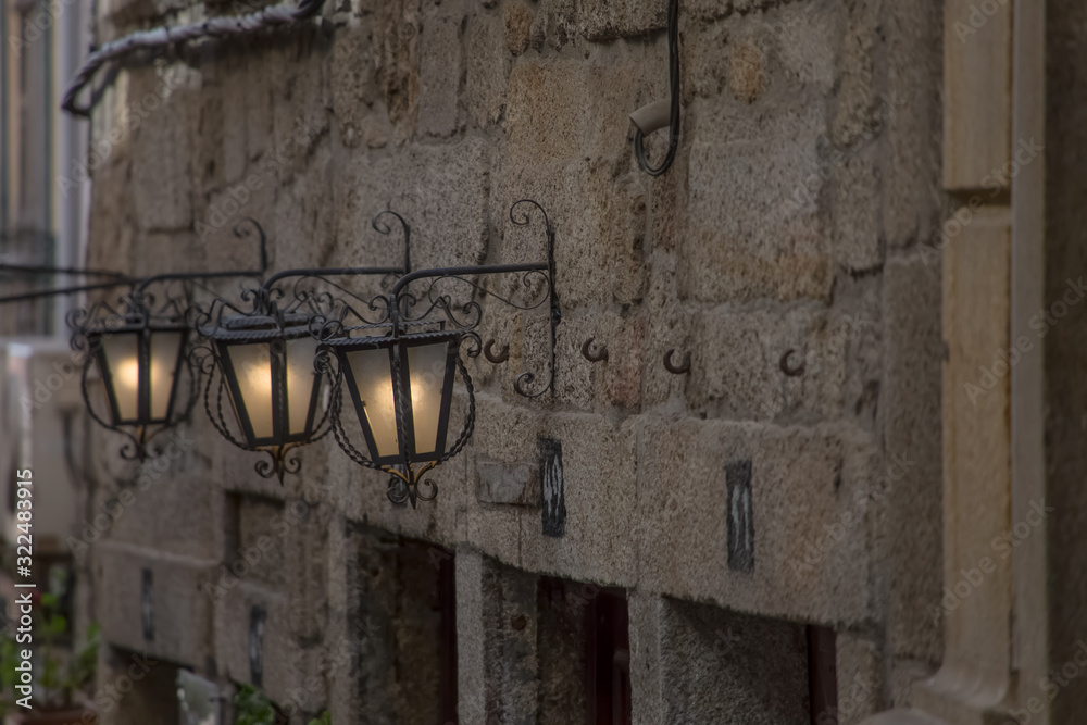 Detailed view of classic stone facade with three street retro wall lamps, on metal material, ornamented and with light on