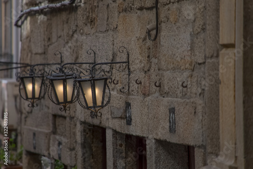 Detailed view of classic stone facade with three street retro wall lamps, on metal material, ornamented and with light on