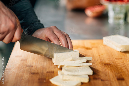 Papier peint Chef's Hands Slicing Tofu Cheese with Knife on a Wooden Cutting Board