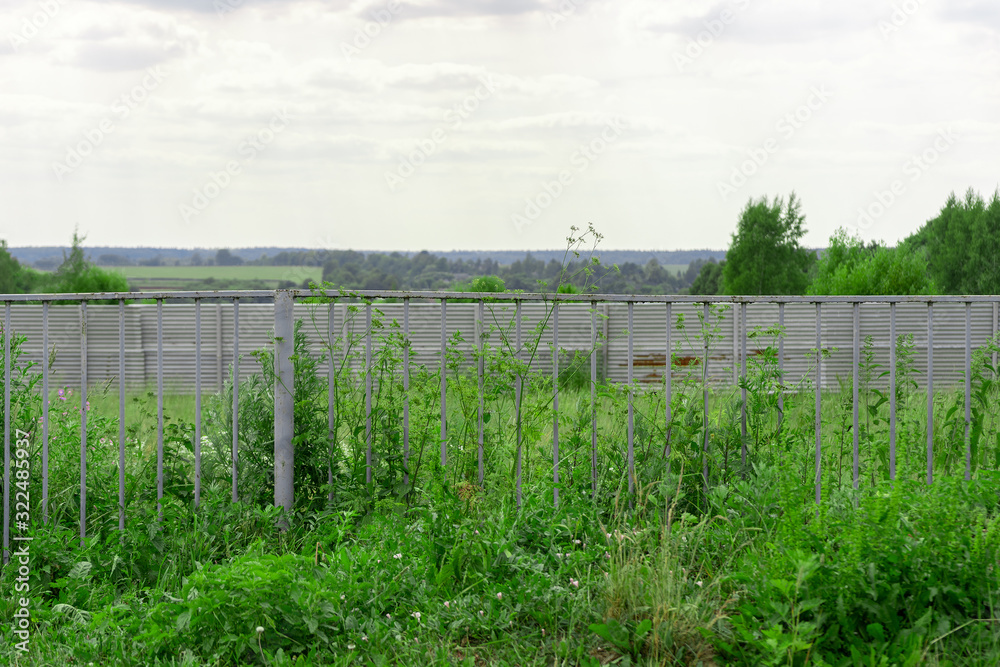 A green field and trees behind an old metal fence