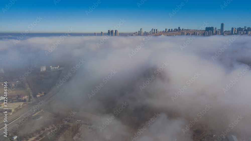 Landscape over the clouds in foggy weather. Hills of buildings in foggy weather. The drone and the top of the fog layer. Buildings in the fog. Landscape over the clouds in foggy weather. Hills of buildings in foggy weather. The drone and the top of the fog layer. Buildings in the fog.