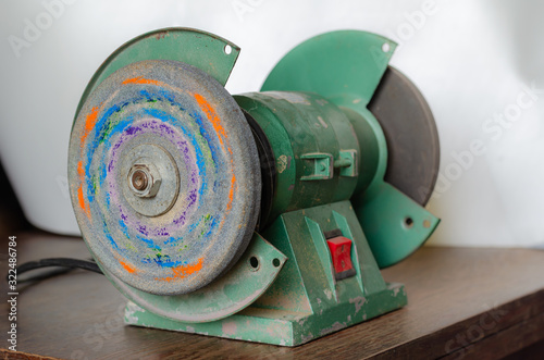 Dirty Electric emery on the table. Used electric emery with traces of paint on the emery wheel. Side view. Selective focus. Without people.