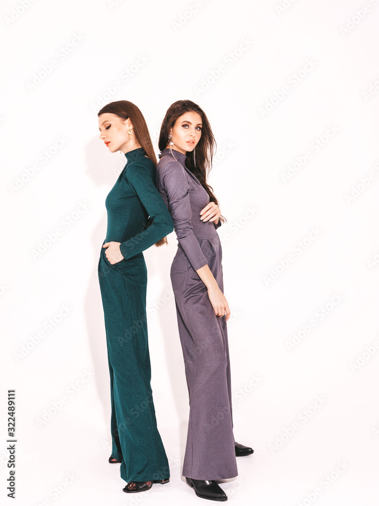 Two young beautiful brunette girls in nice trendy summer suit clothes.Sexy carefree women posing near white wall in studio.Fashionable models with bright evening makeup.They hug and touch each other Two young beautiful brunette girls in nice trendy summer suit clothes.Sexy carefree women posing near white wall in studio.Fashionable models with bright evening makeup.They hug and touch each other