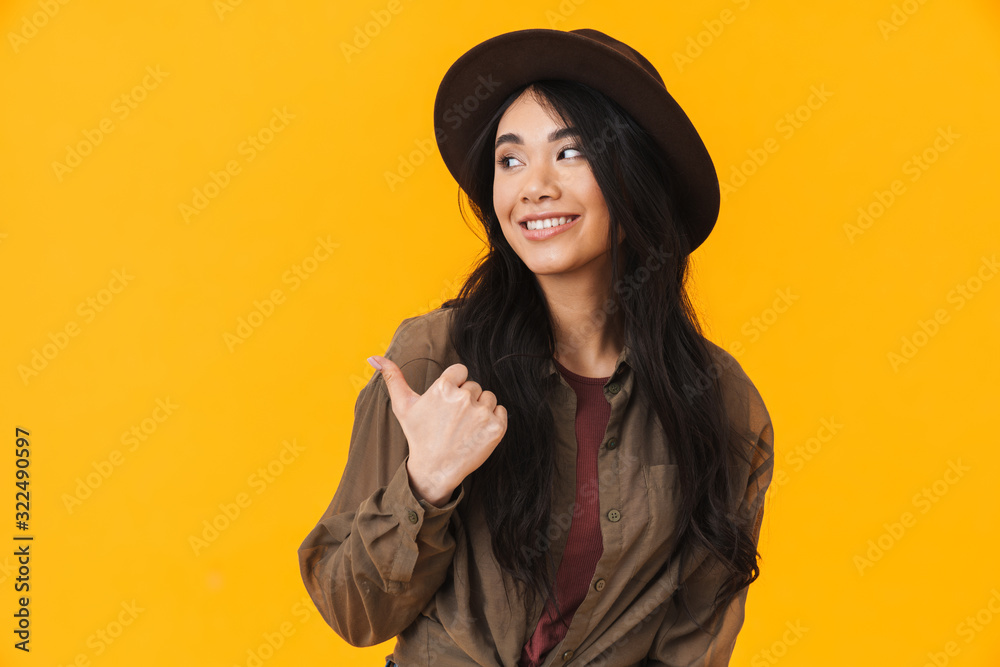 Image of young asian woman wearing hat smiling and pointing finger Image of young asian woman wearing hat smiling and pointing finger