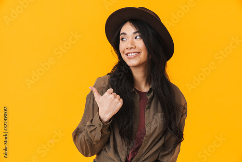 Image of young asian woman wearing hat smiling and pointing finger © Drobot Dean