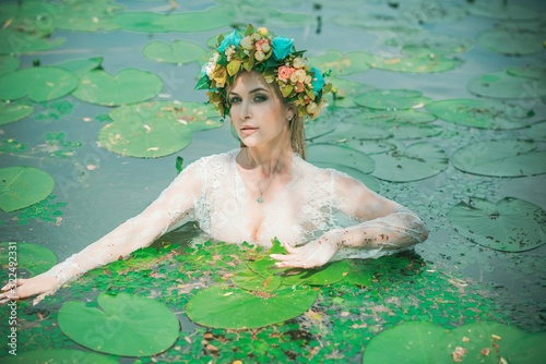 Romantic woman in flower hoop at hair, lace transparent dress in lake 