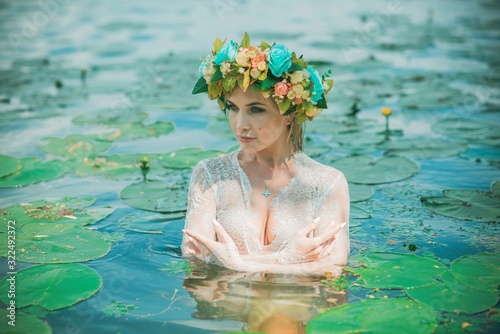 Romantic woman in flower hoop at hair, lace transparent dress in lake 