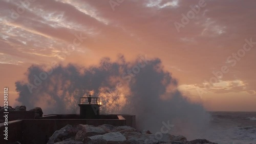 Schizzi e spruzzi del mare che si infrangono sul faro del porto al tramonto. Super slow motion. photo