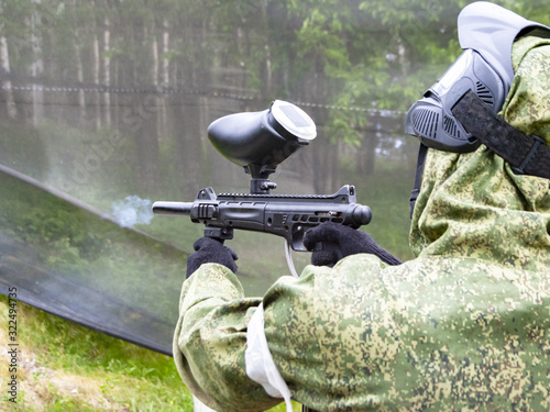 man playing paintball shoots a machine gun at a training ground on a summer day