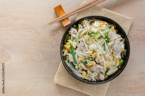 top view of stir fried bean sprout with pork and egg in a ceramic bowl on wooden table. asian homemade style food concept.