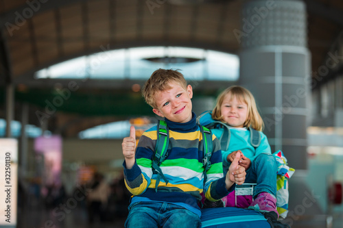 happy cute boy and girl wait in airport, kids sit on luggage