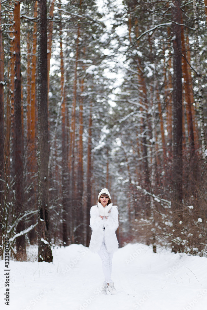A beautiful pretty young girl with curly hair and a snow-white smile in a white warm fur coat is walking and fooling around in the winter forest against the background of snow and trees, enjoying A beautiful pretty young girl with curly hair and a snow-white smile in a white warm fur coat is walking and fooling around in the winter forest against the background of snow and trees, enjoying