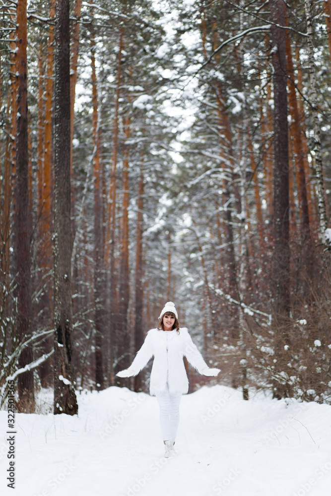 A beautiful pretty young girl with curly hair and a snow-white smile in a white warm fur coat is walking and fooling around in the winter forest against the background of snow and trees, enjoying A beautiful pretty young girl with curly hair and a snow-white smile in a white warm fur coat is walking and fooling around in the winter forest against the background of snow and trees, enjoying