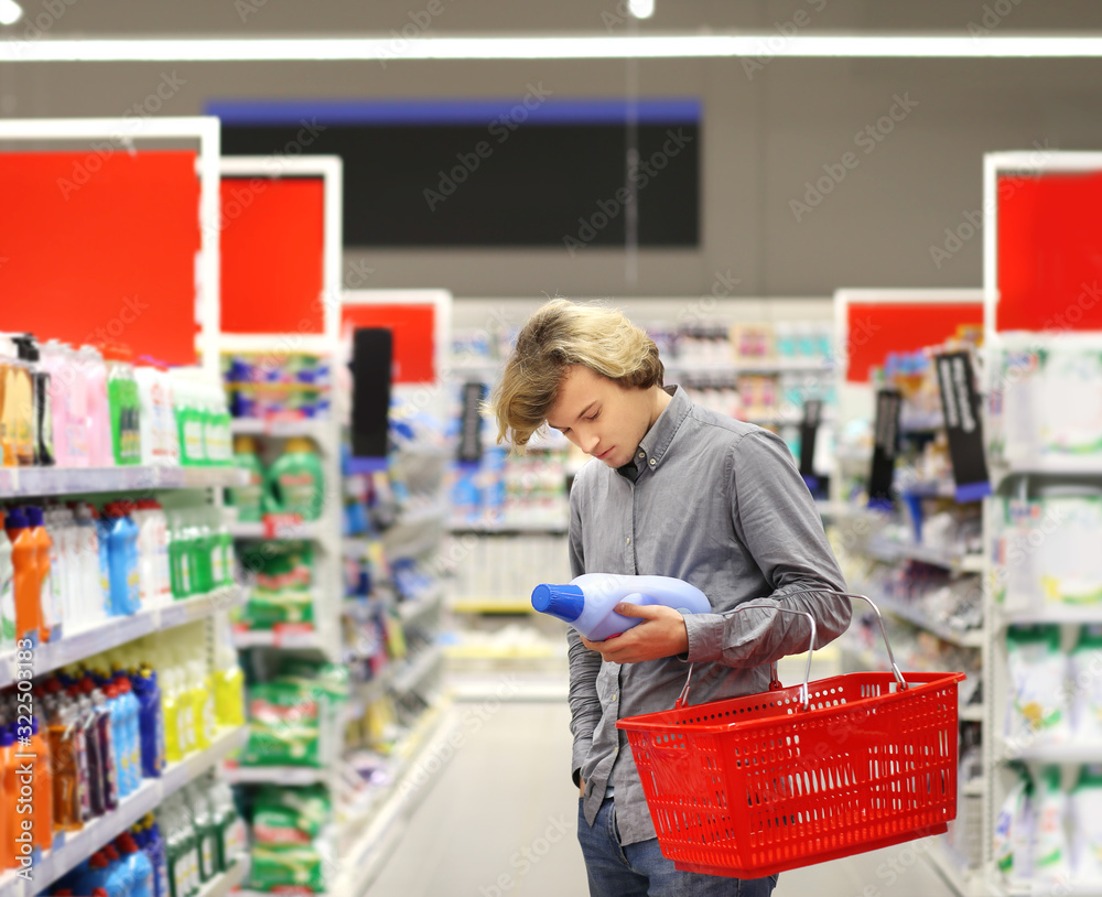 Man shopping in supermarket reading product information.(washing powder,detergent)	