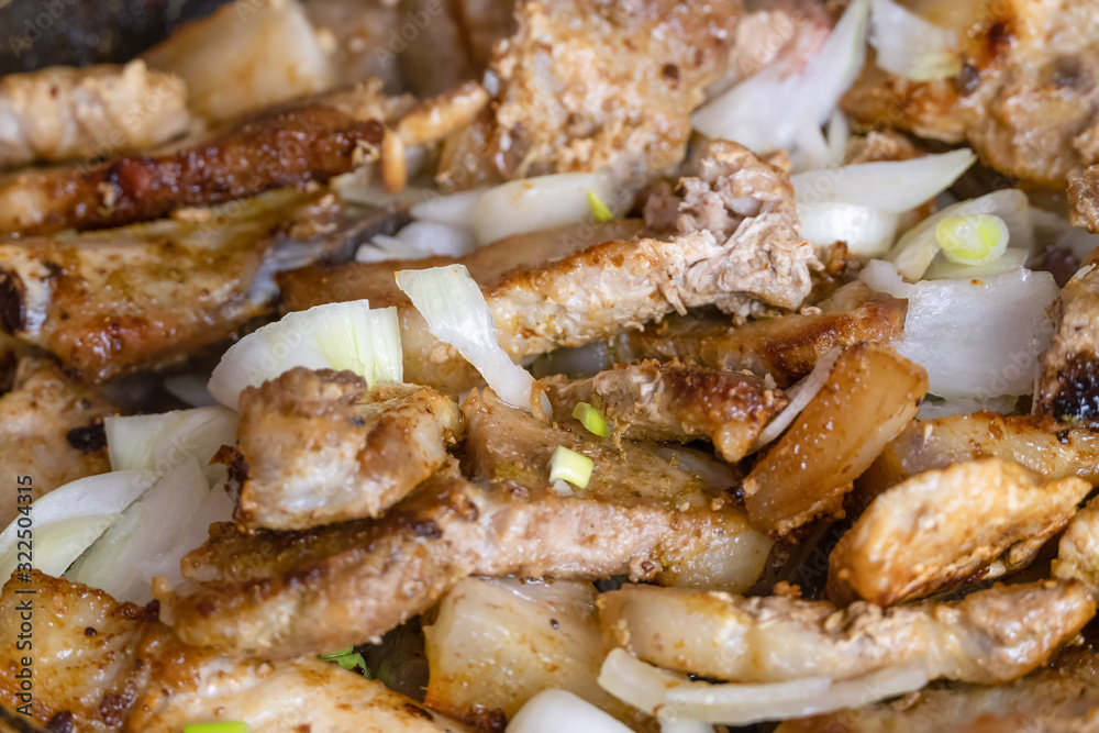 Fried pieces of meat with onions are fried in a pan close up