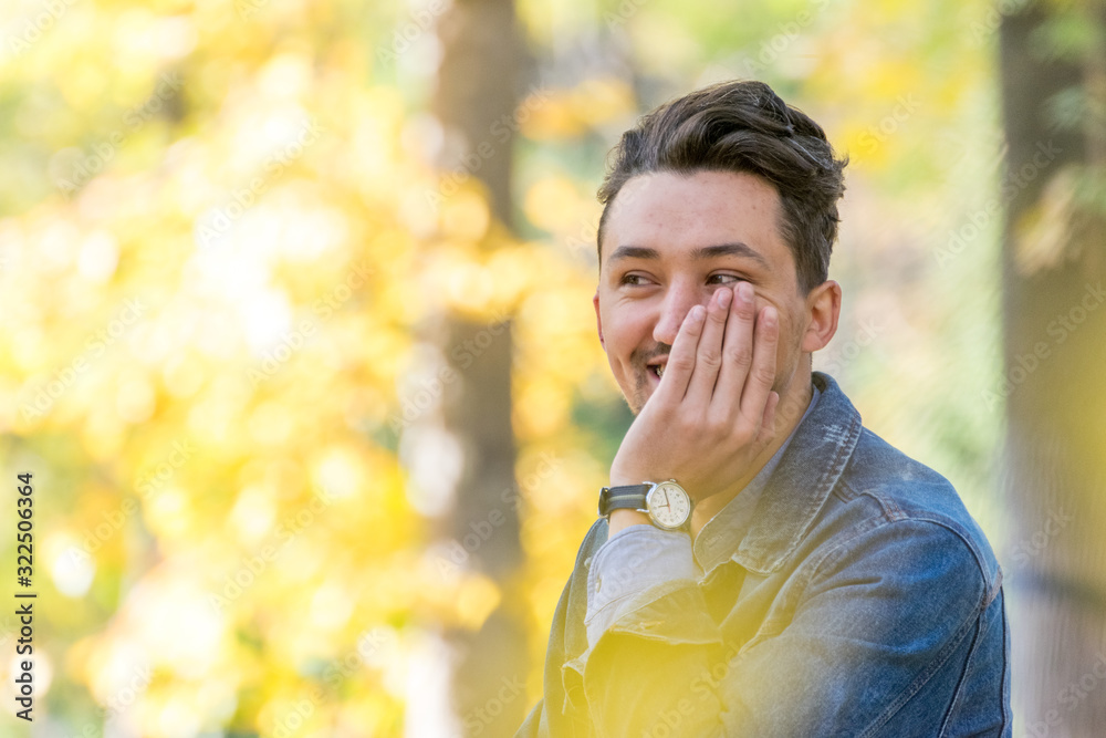 Handsome young man looking at the camera. Portrait of laughing confident and successful young man with a denim jacket and blue shirt outside. Happy guy smiling