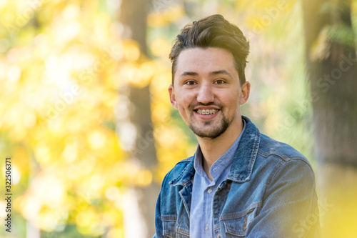 Handsome young man looking at the camera. Portrait of laughing confident and successful young man with a denim jacket and blue shirt outside. Happy guy smiling