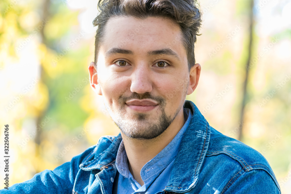 Handsome young man looking at the camera. Portrait of laughing confident and successful young man with a denim jacket and blue shirt outside. Happy guy smiling