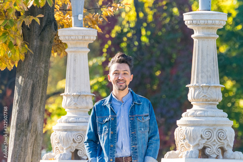 Obraz na płótnie Handsome young man looking at the camera. Portrait of laughing confident and successful young man with a denim jacket and blue shirt outside. Happy guy smiling w salonie