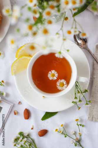 Cute Provencal style still life with herbal tea and flowers. Hot tea with chamomile and lemon for the treatment or prevention of colds or flu using the folk method. Light, romantic photo.