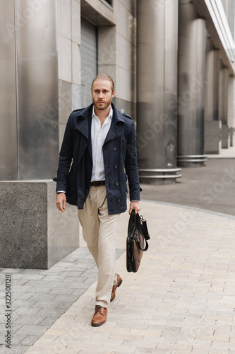 Image of handsome young confident businessman walking on city street