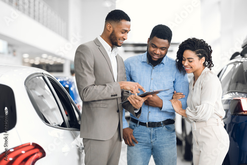 Salesman Offering Couple A Car Standing In Auto Rental Office photo