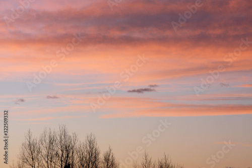 Dreamy evening sky in pastel tones with fluffy pink orange clouds at sunset over silhouette of hill country