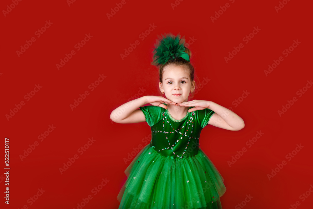 Beautiful little girl princess dancing in luxury green dress isolated on red background. Carnival party with costumes