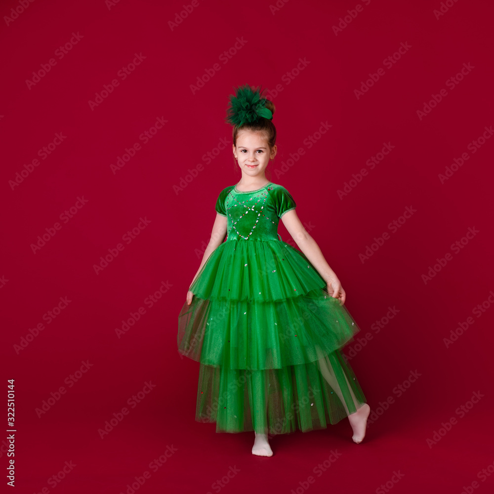 Beautiful little girl princess dancing in luxury green dress isolated on red background. Carnival party with costumes Beautiful little girl princess dancing in luxury green dress isolated on red background. Carnival party with costumes