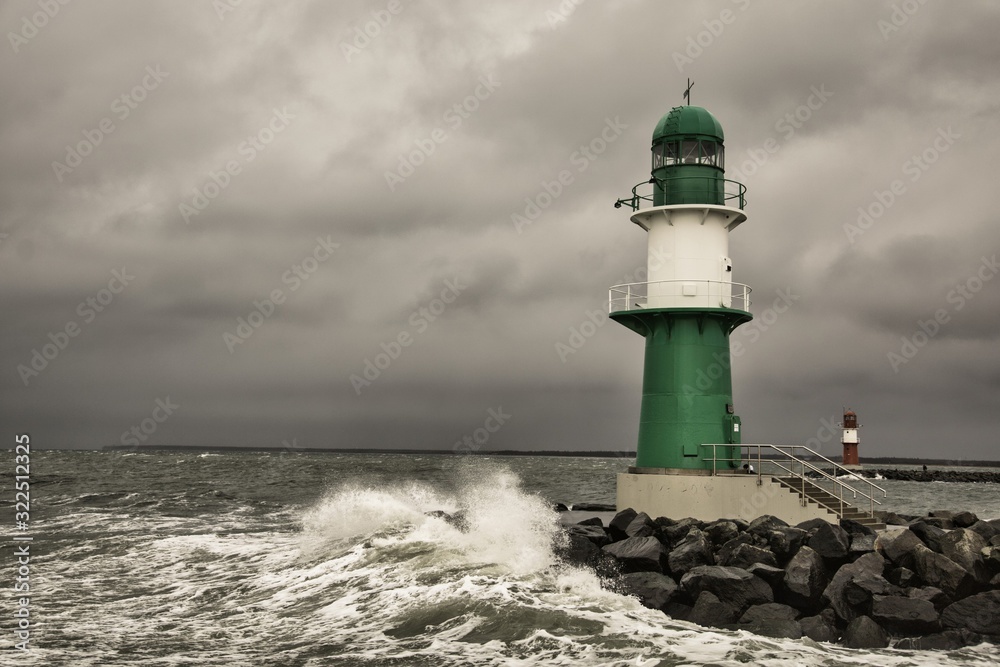 Lighthouse on the pier in Warnemuende during storm the waves break on the pier - Baltic Sea in Germany