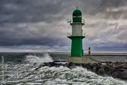 Lighthouse on the pier in Warnemuende during storm the waves break on the pier - Baltic Sea in Germany