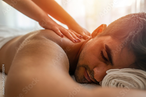 Masseur doing back massage on man body in the spa salon. Beauty treatment concept. Girl in a T-shirt doing a massage to a guy. Candles in the foreground. Man lying on the table on a white background.