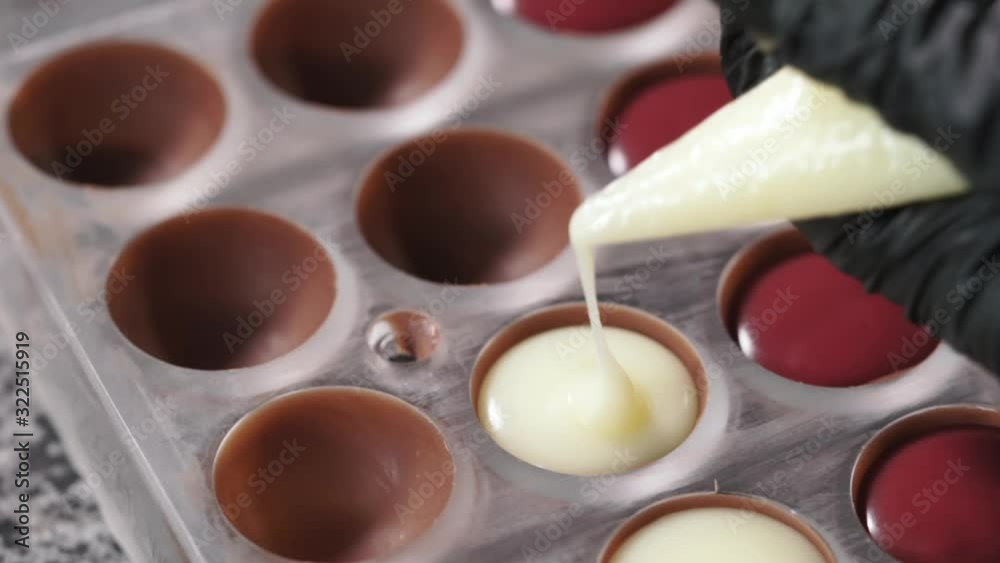 Confectioner filling polycarbonate bonbon mold with creamy chocolate from the piping bag