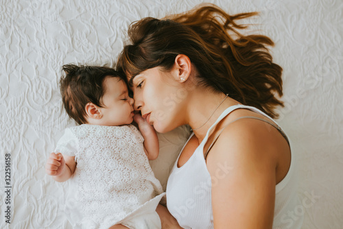 baby lying in bed next to her mom who is hugging her - family concept