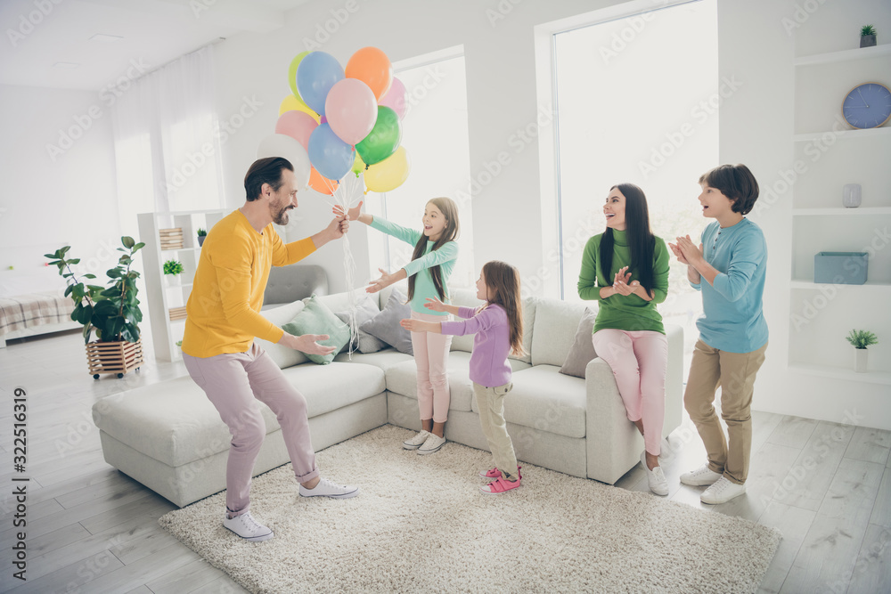 Full body photo of energetic fun people celebrate family day dad daddy give present gift surprise his three small schoolgirls mom mommy sit cozy couch clap hands enjoy fest in house room