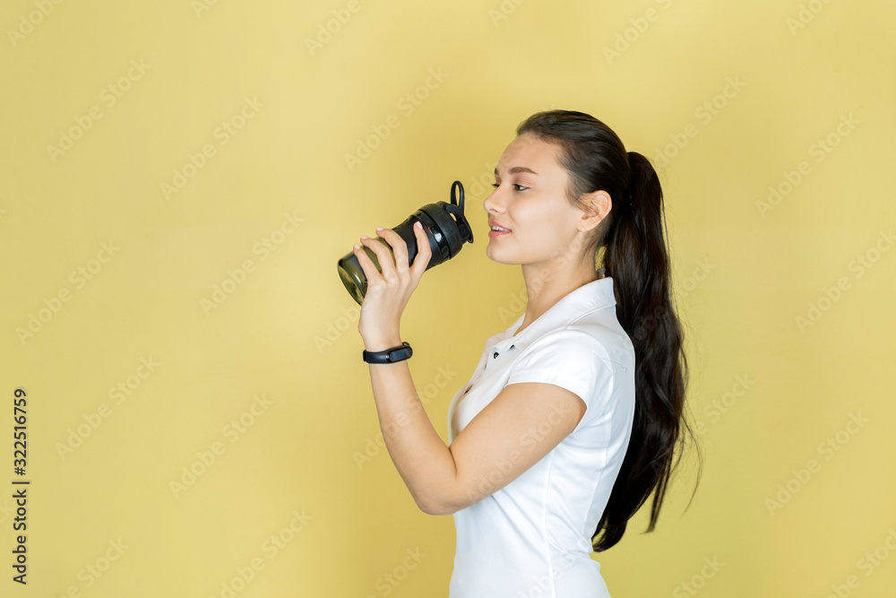 Obraz premium Beautiful young woman the brunette in white t-shirt with a fitness shaker drinking water. Sport fitness. copy space