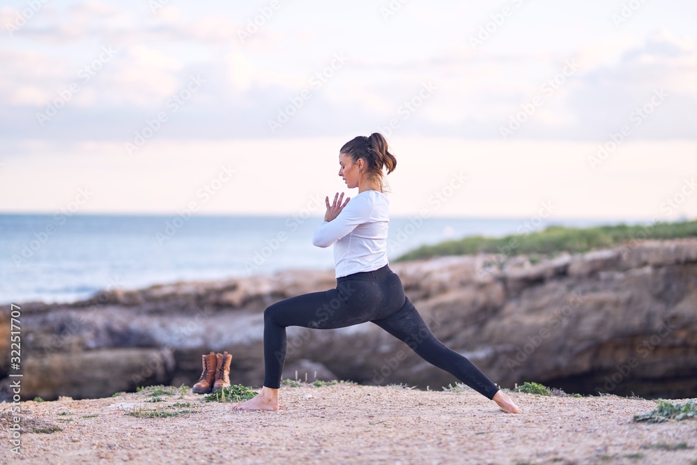 Young beautiful sportwoman practicing yoga. Coach teaching warrior pose at the beach