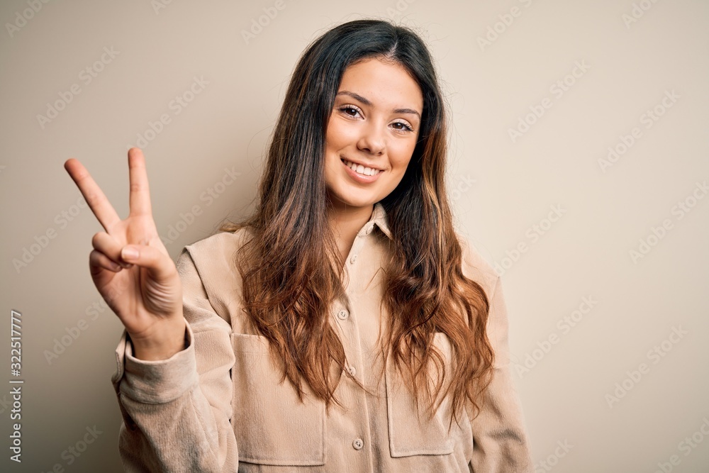 Young beautiful brunette woman wearing casual shirt standing over white background showing and pointing up with fingers number two while smiling confident and happy. Young beautiful brunette woman wearing casual shirt standing over white background showing and pointing up with fingers number two while smiling confident and happy.
