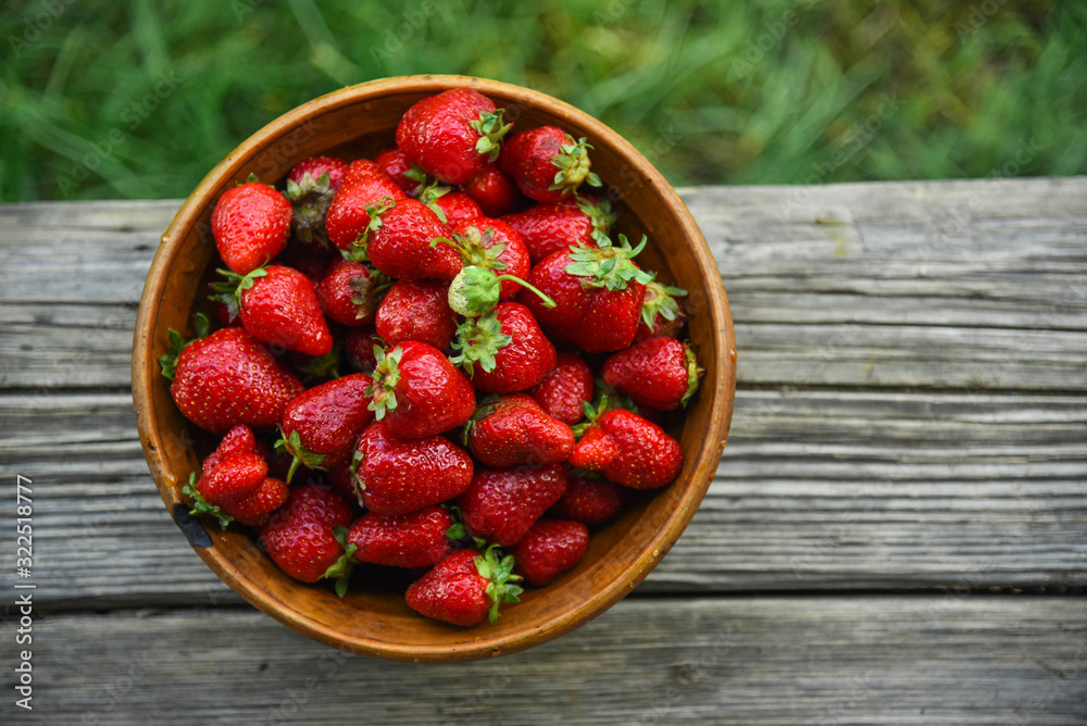 Red fresh strawberries in a old rustic wooden bowl. Raw food on a green background. Red fresh strawberries in a old rustic wooden bowl. Raw food on a green background.
